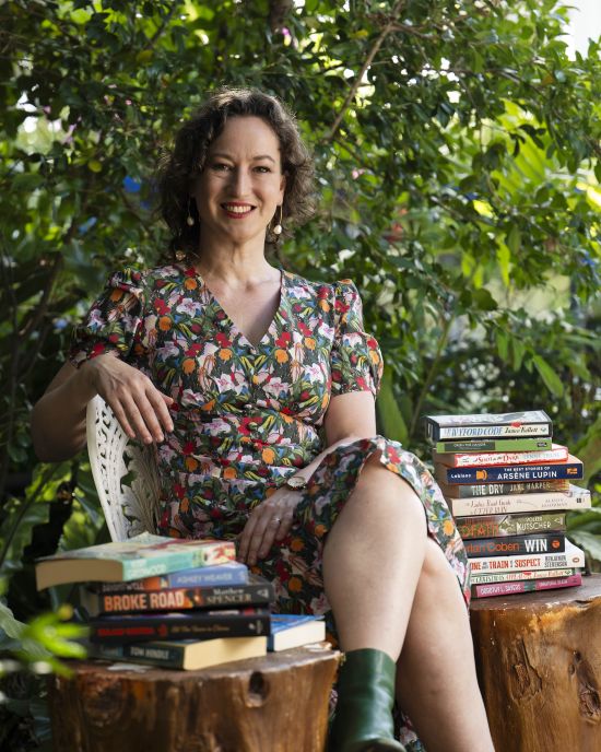Woman sitting on a log with books, surrounded by greenery