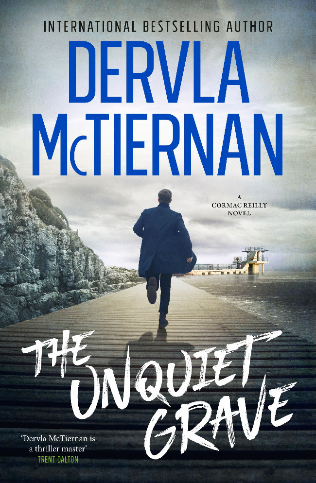 Book cover of 'The Unquiet Grave' by Dervla McTiernan with a person walking on a path towards the sea.